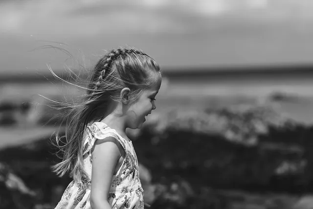 Black and white photo of a girl on the beach, her hair blowing in the sea breeze