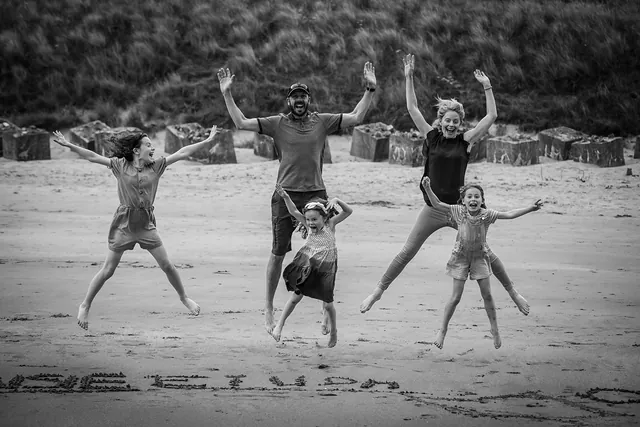 Black and white photo of a family jumping for joy on the beach