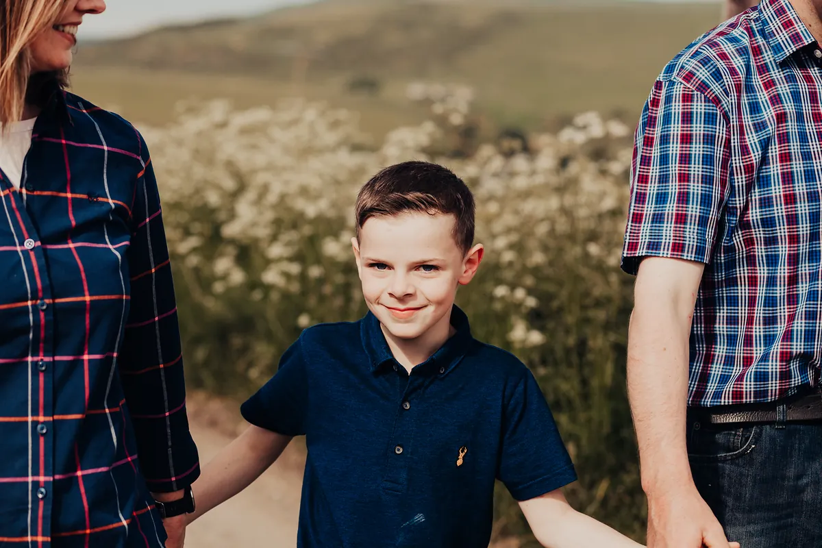 A boy smiling between his parents in a meadow
