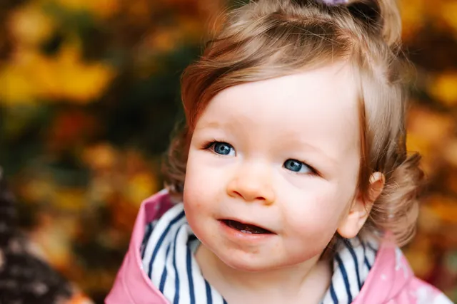 A smiling toddler with bright blue eyes against warm autumn colours