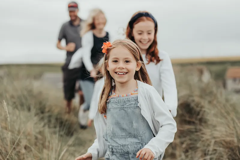 A girl running through the dunes towards the camera with her family behind her