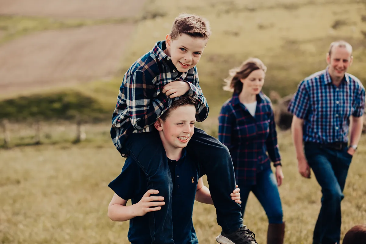 A family walking through a field together, one brother giving the other a piggyback