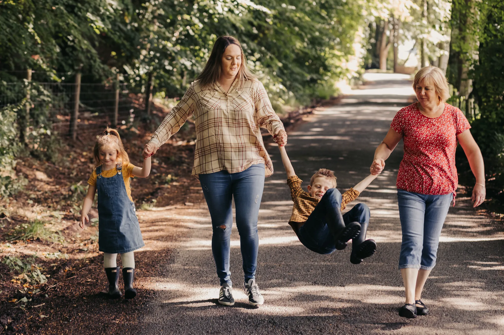 A family walking down a sunlit country lane, swinging their little boy between them