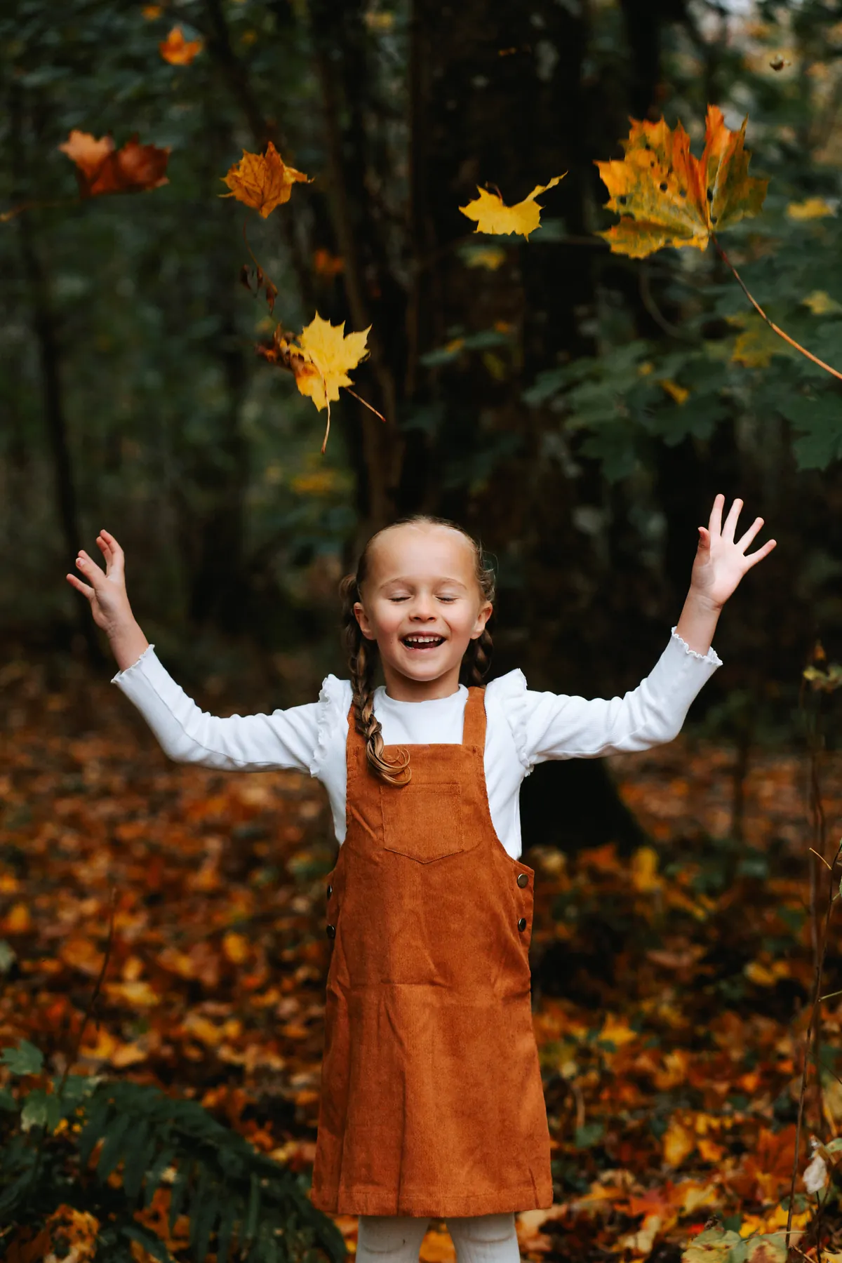 A girl in an orange pinafore throwing autumn leaves into the air
