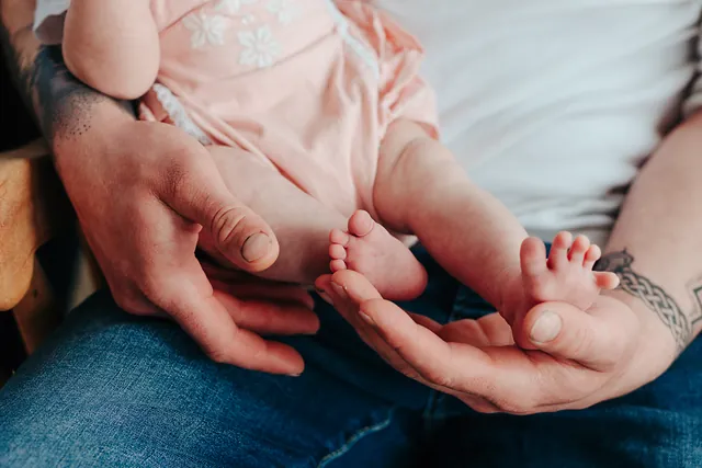 A newborn baby's tiny feet cradled in her dad's hands
