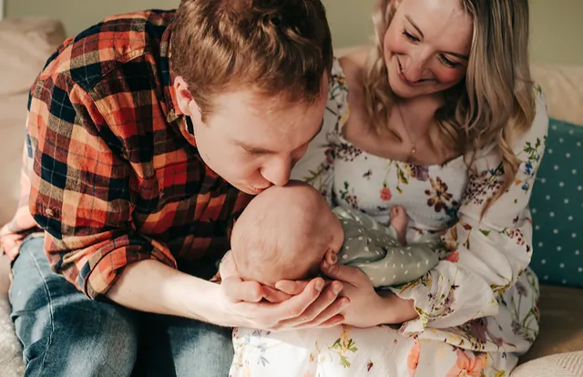 A dad kissing his newborn baby's head as mum looks on