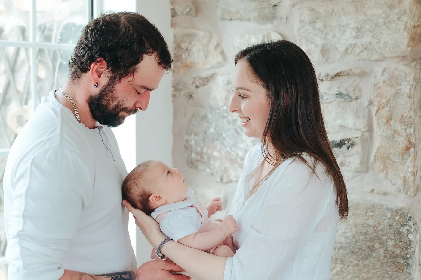 Parents gazing down at their newborn baby in a bright room with a stone wall