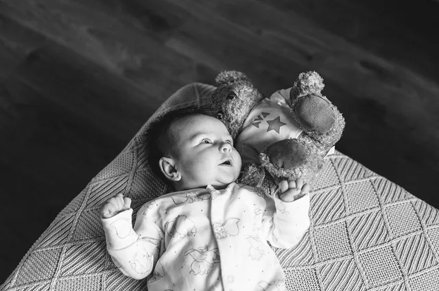 Black and white photo of a newborn baby lying beside a teddy