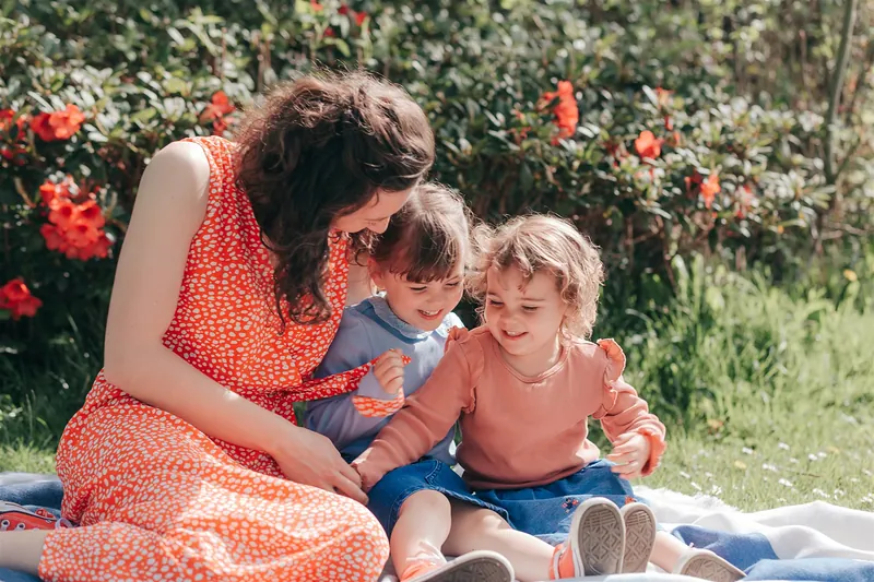 A mum cuddling her two children on a picnic blanket in a summer garden