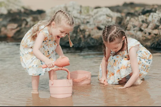 Two sisters playing in a rockpool with a pink bucket