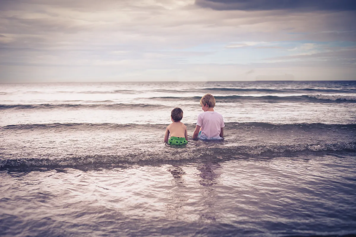 Two children paddling in the sea under a soft sky