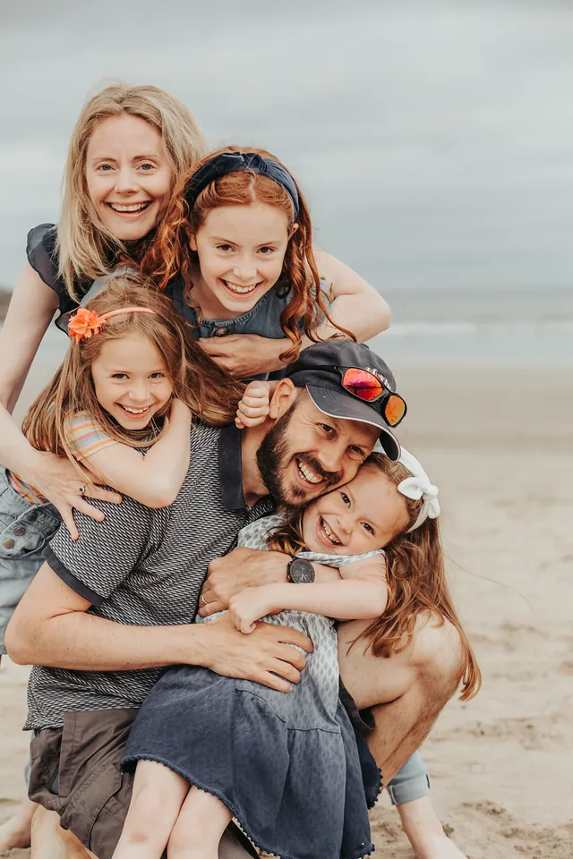 Three sisters piled on their dad on the beach, all laughing
