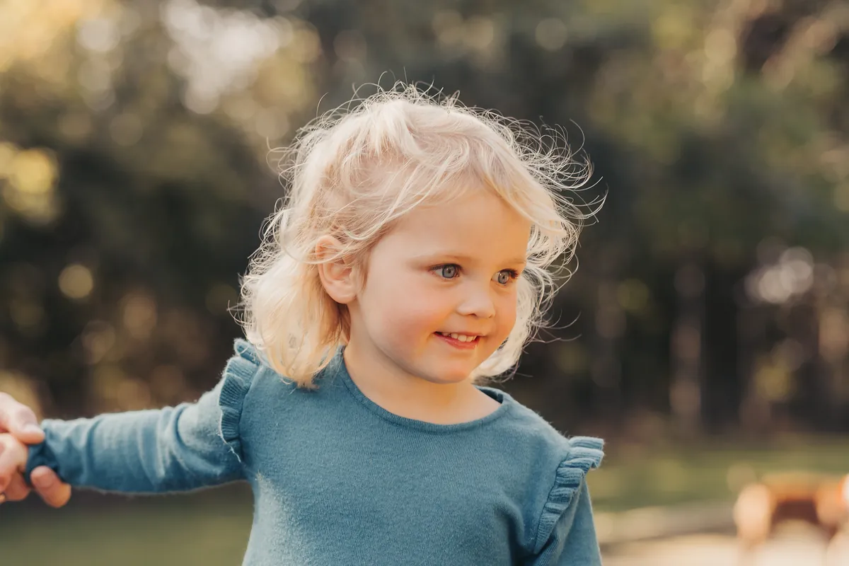 A toddler with sunny blonde curls smiling outdoors