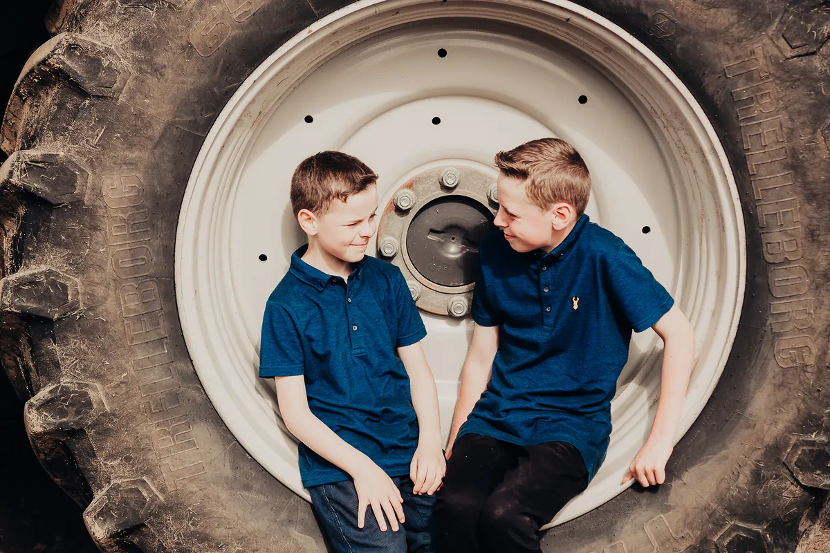 Two brothers sitting inside a giant tractor tyre, sharing a grin