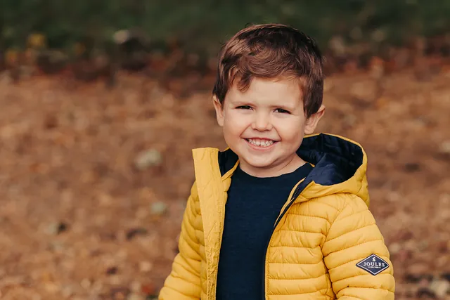 A little boy in a yellow jacket laughing among autumn leaves