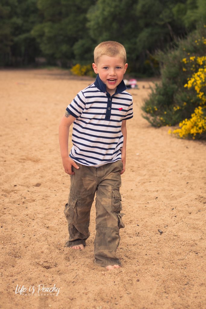 Boy walking on sand looking at camera. Loch Morlich, Highlands. Family photography, Aberdeenshire and Moray
